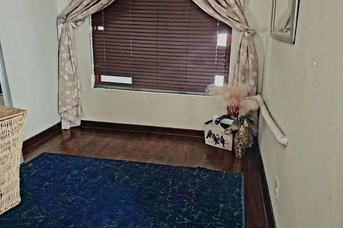 A bedroom space featuring timber flooring, venetian blinds, and a wall-mounted grab rail, with neutral wall finishes.