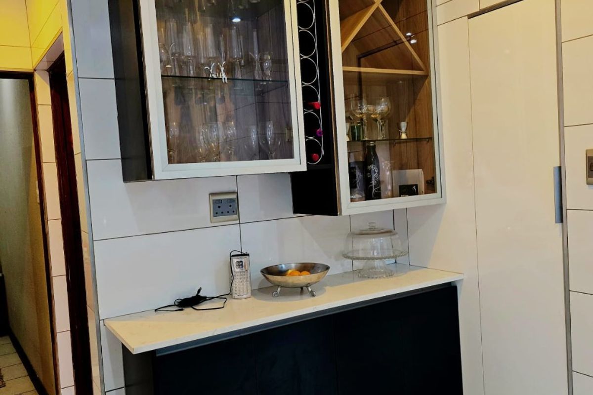 A modern kitchen area featuring sleek black cabinetry, glass-fronted display units, a built-in wine rack, and high-gloss tiled finishes.