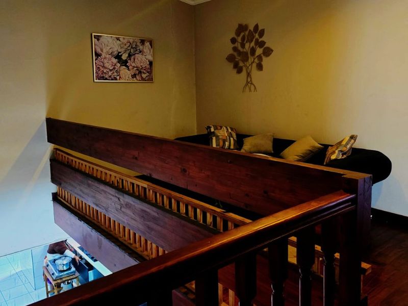 An elevated mezzanine hallway area featuring a wooden balustrade overlooking the lower level, with warm recessed lighting and wooden flooring.