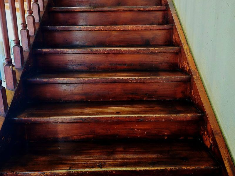 A traditional wooden staircase featuring a classic balustrade, showing significant wear to the wood finish on the treads.