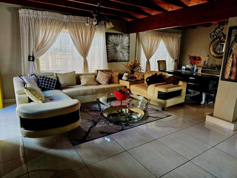 Spacious living area featuring exposed timber ceiling beams, large windows allowing natural light, and neutral tiled flooring throughout.