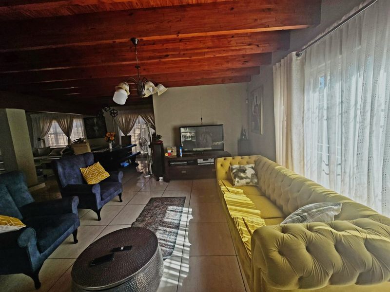 Spacious living room featuring exposed timber ceiling beams, tiled flooring, and large sliding glass doors that provide ample natural light.