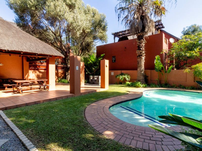 Outdoor entertainment area featuring a swimming pool with brick coping, a covered thatched lapa, and a built-in braai set within a private garden.