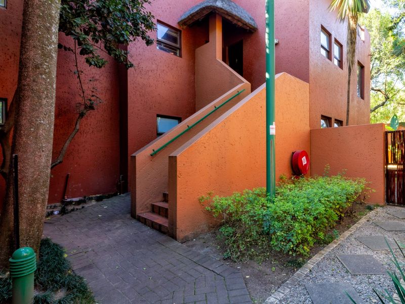 Exterior view of an apartment building entrance featuring a thatched roof canopy, concrete staircase, and paved walkway access.