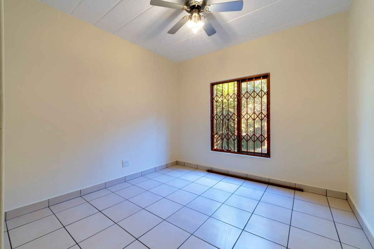 An empty bedroom featuring tiled flooring, a ceiling fan, and a window fitted with a security gate.