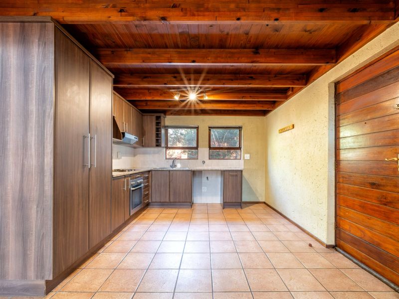 A functional kitchen featuring dark wood cabinetry, built-in oven and hob, tiled flooring, and a distinctive exposed timber beam ceiling.