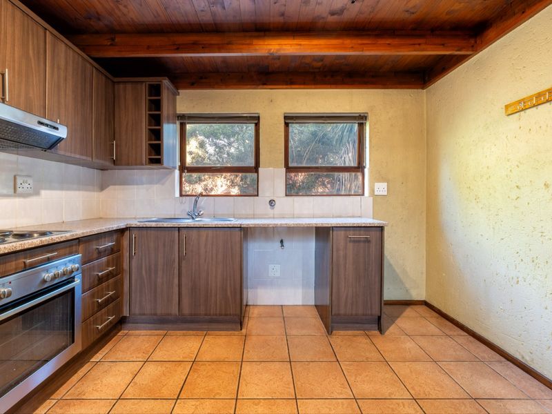 A functional kitchen featuring built-in cabinetry, a stainless steel oven with extractor, tiled flooring, and a distinctive timber-beamed ceiling.