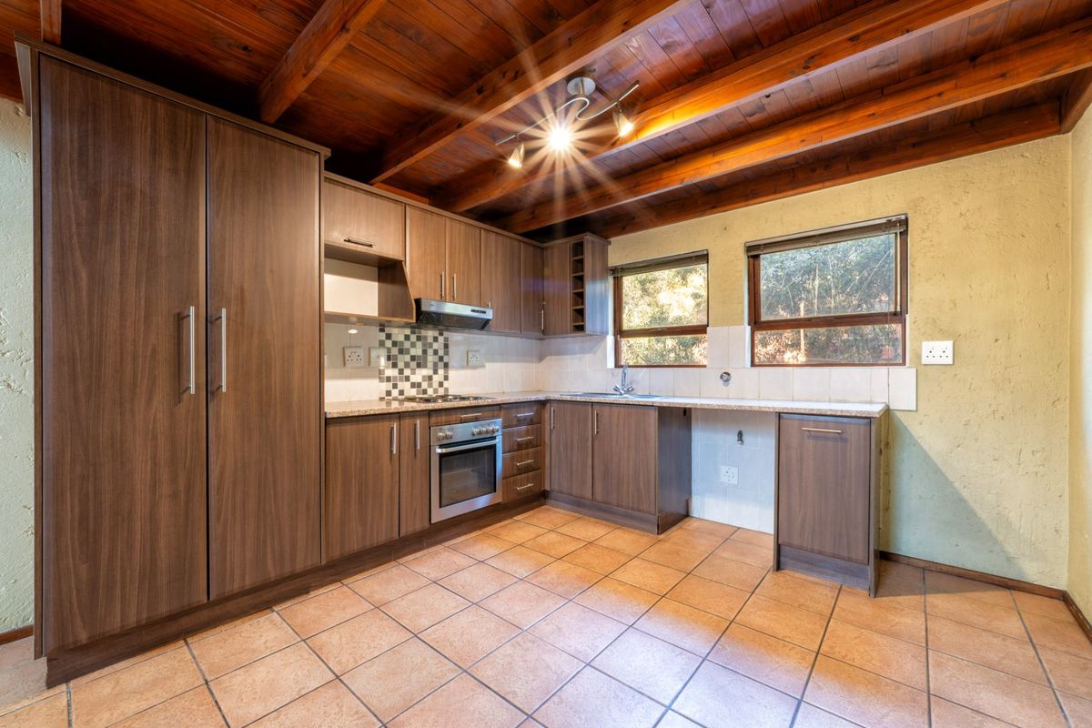 A functional kitchen featuring wood-finish cabinetry, granite countertops, built-in oven and hob, tiled flooring, and exposed timber ceiling beams.