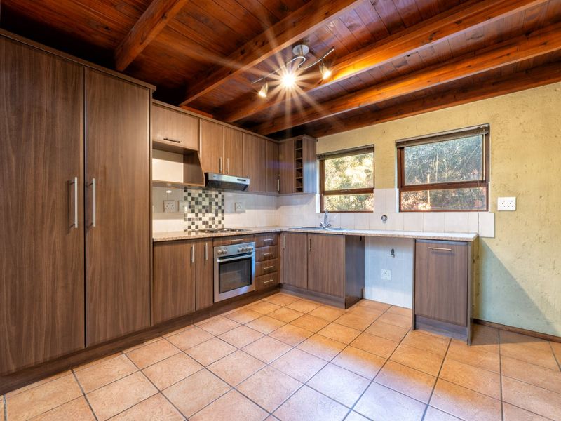A functional kitchen featuring wood-finish cabinetry, granite countertops, built-in oven and hob, tiled flooring, and exposed timber ceiling beams.