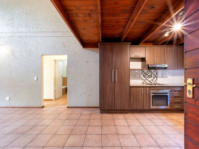Open-plan kitchen area featuring dark wood cabinetry, built-in oven, hob, extractor fan, tiled flooring, and exposed timber ceiling beams.