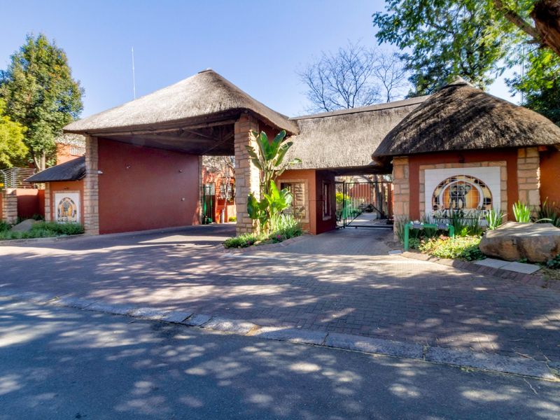 The property features a secure entrance with a distinctive thatch roof, stone pillars, and a paved driveway leading into the complex.