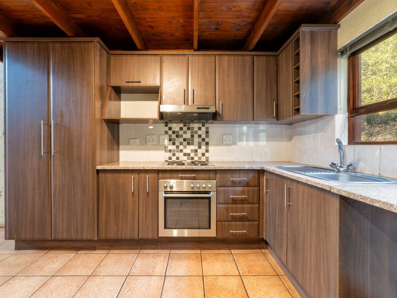 A functional kitchen featuring dark wood cabinetry, granite-look laminate countertops, built-in oven and hob, and distinctive exposed timber ceiling beams.