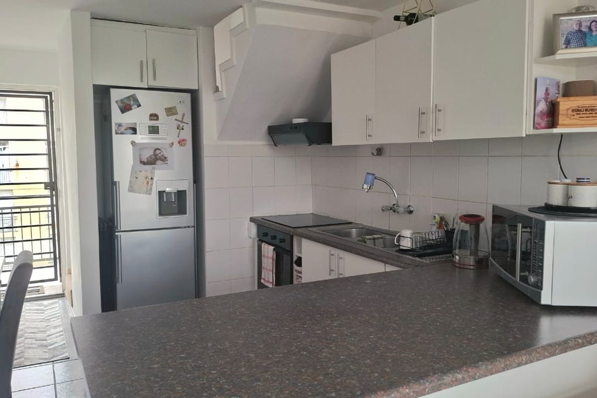Compact kitchen featuring white cabinetry, laminate countertops, built-in oven and hob, tiled backsplash, and direct access to an outdoor balcony area.