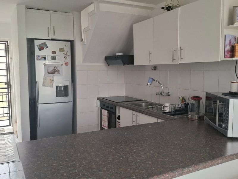 Compact kitchen featuring white cabinetry, laminate countertops, built-in oven and hob, tiled backsplash, and direct access to an outdoor balcony area.