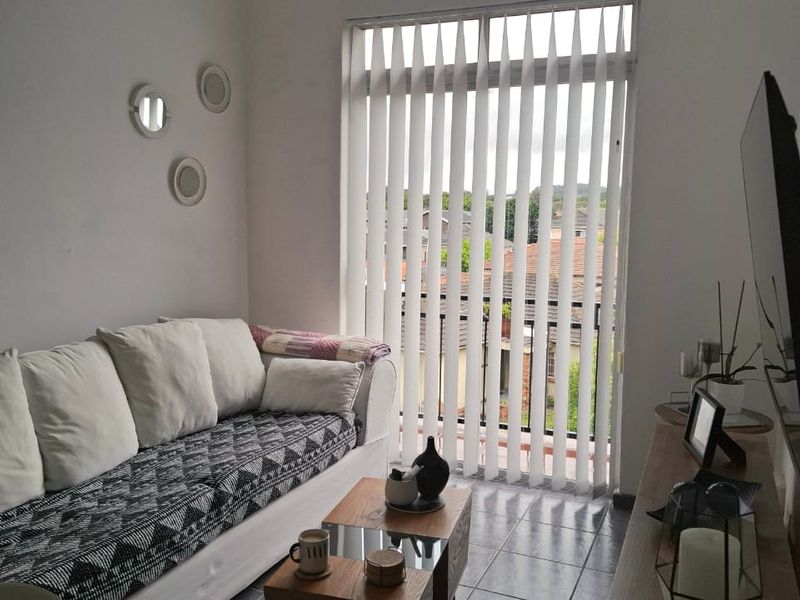 A living room featuring tiled flooring and vertical blinds, with direct access to a balcony.