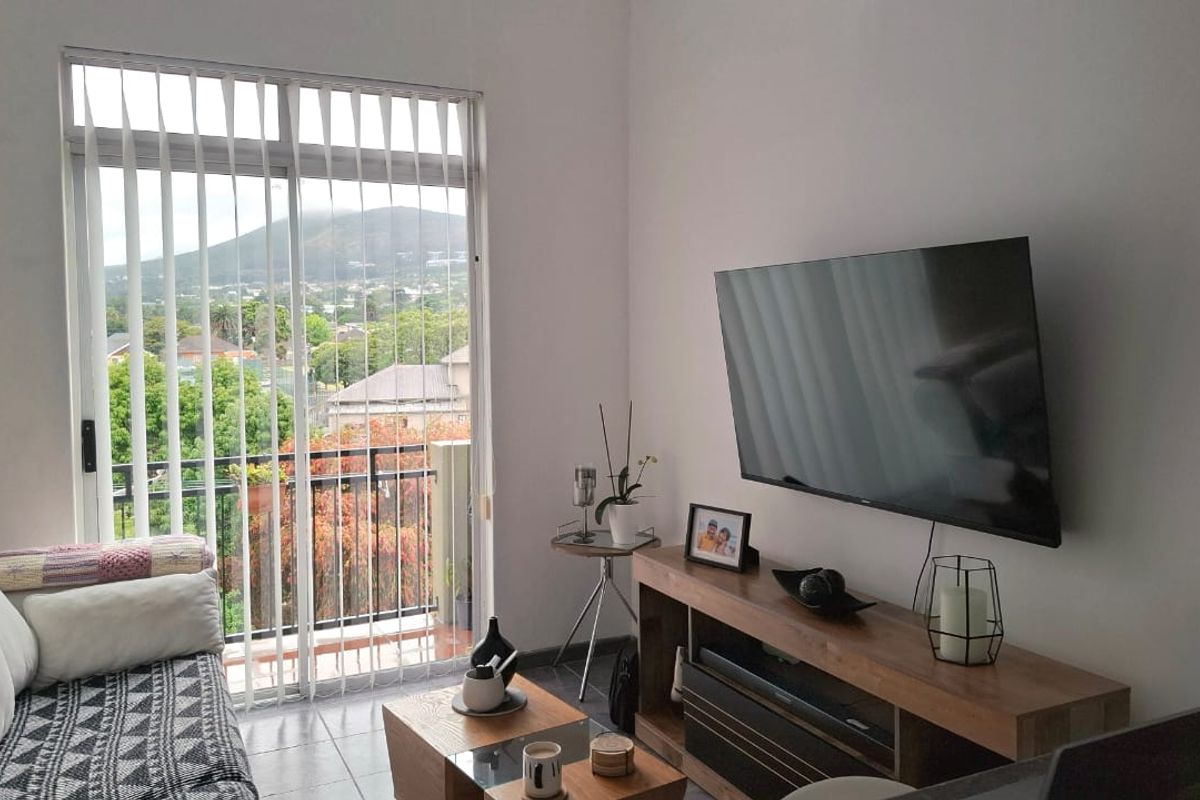 A bright living room featuring tiled flooring and a large sliding glass door that provides access to a balcony with scenic views.
