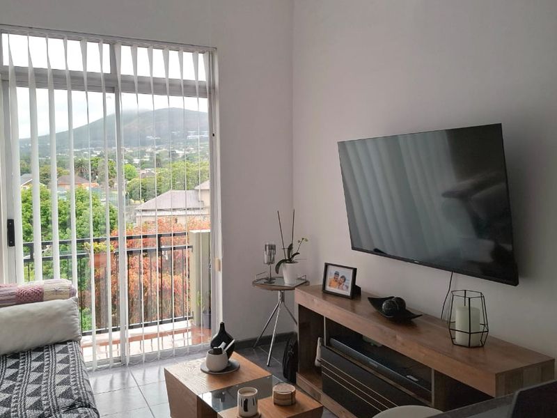 A bright living room featuring tiled flooring and a large sliding glass door that provides access to a balcony with scenic views.