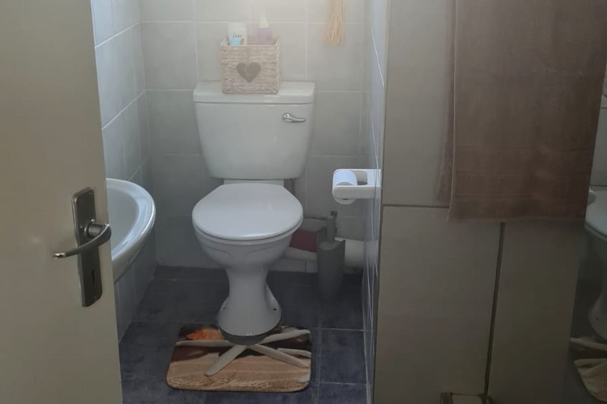 A functional bathroom featuring a toilet, wall-mounted basin, and a shower enclosure with tiled finishes throughout.