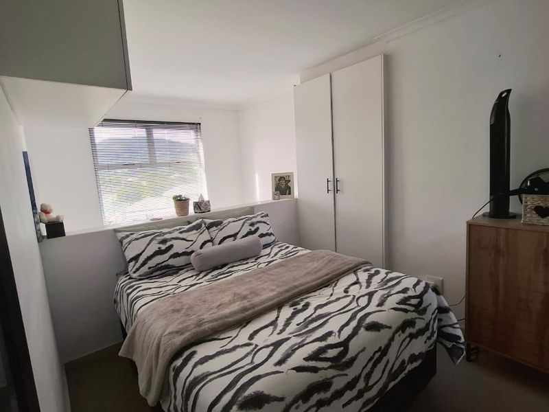 A compact bedroom featuring a built-in wardrobe, overhead storage cabinetry, and venetian blinds, providing functional storage and natural light.