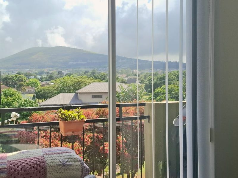 A view from an interior space through a sliding glass door, showcasing a scenic outlook of trees and a distant mountain.