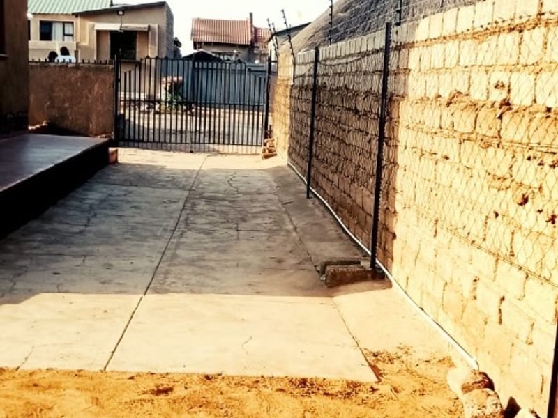 Rear exterior area featuring a concrete driveway, perimeter wall with electric fencing, and a metal gate access point.