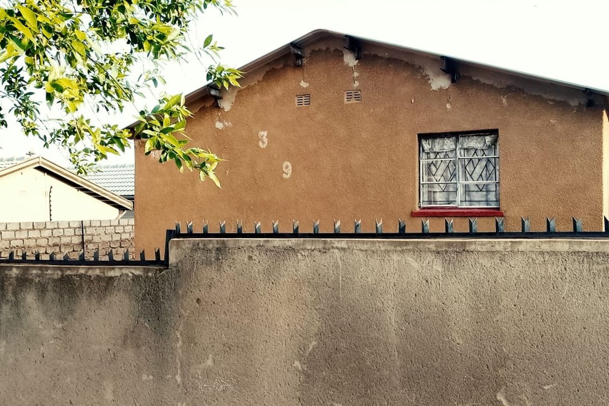Rear view of the property showing a plastered exterior wall with visible paint deterioration and a window fitted with security bars.