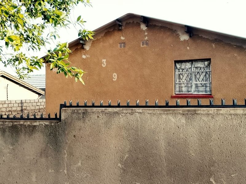 Rear view of the property showing a plastered exterior wall with visible paint deterioration and a window fitted with security bars.