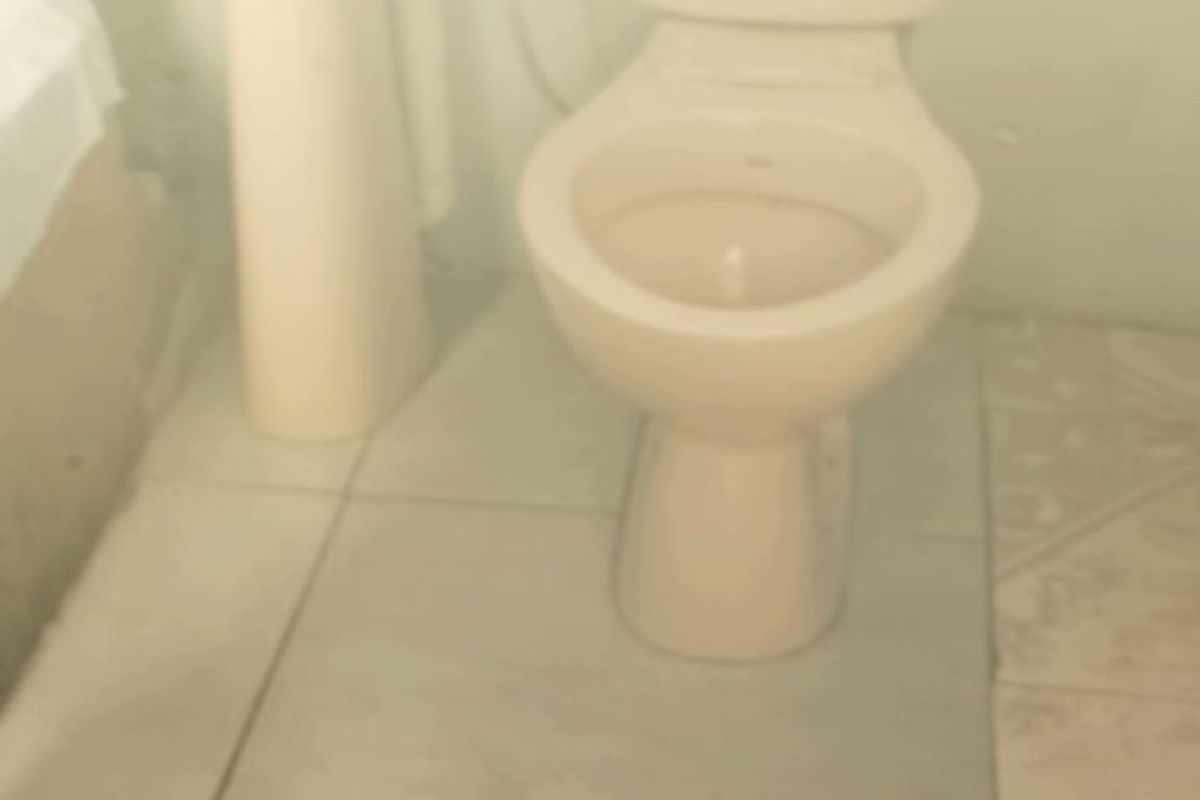 A small bathroom featuring a pedestal basin and toilet with ceramic floor tiling, requiring cosmetic updates and repairs.
