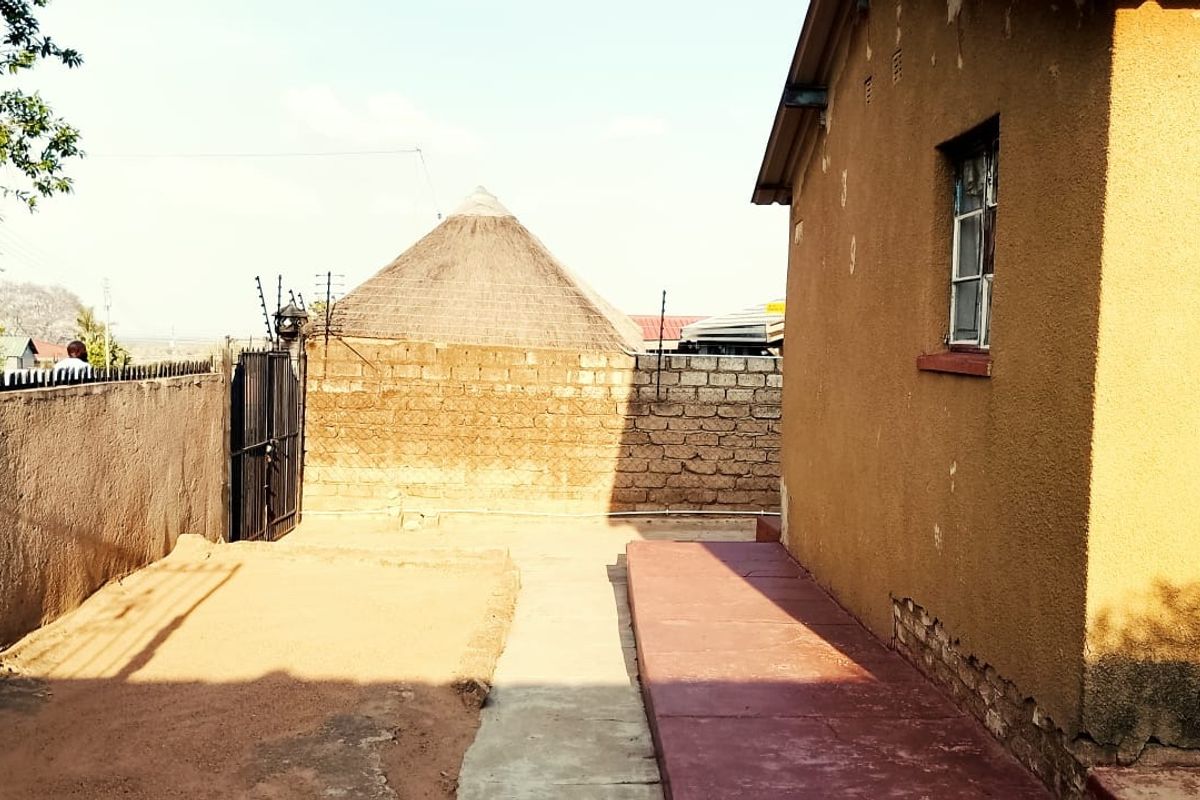 A view of the rear exterior area featuring a concrete pathway, perimeter wall with electric fencing, and a metal gate.