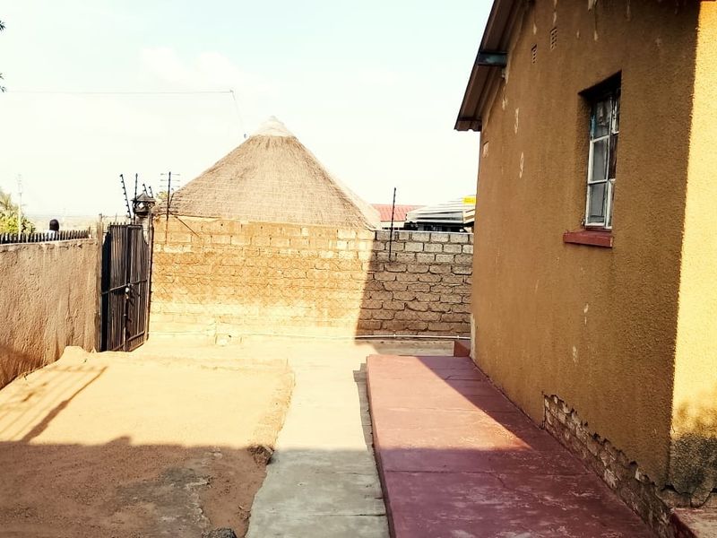 Rear exterior view of the property featuring a concrete pathway, perimeter wall with electric fencing, and a metal gate.