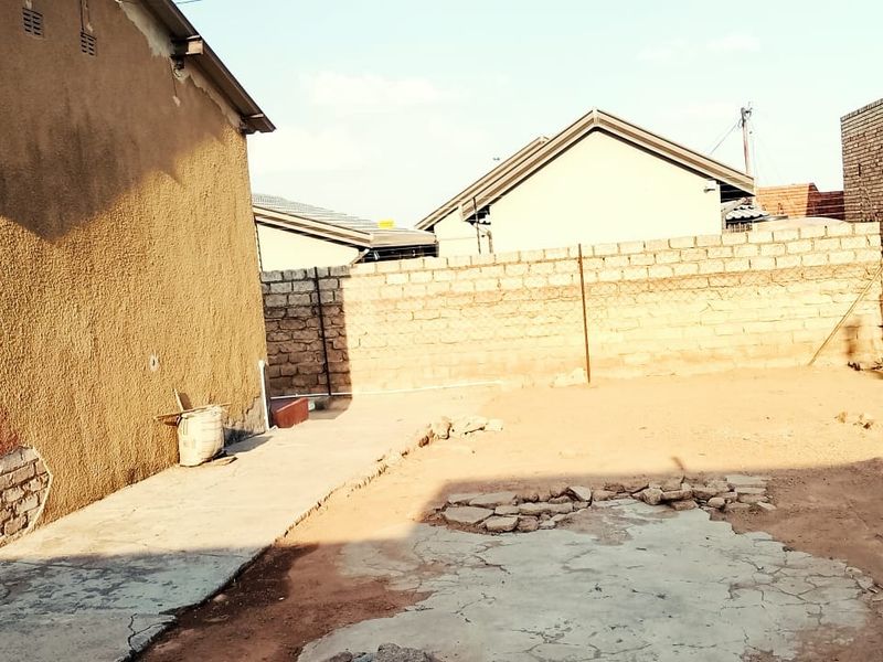 A rear yard area featuring a perimeter brick wall with razor wire and a section of cracked concrete paving requiring maintenance.