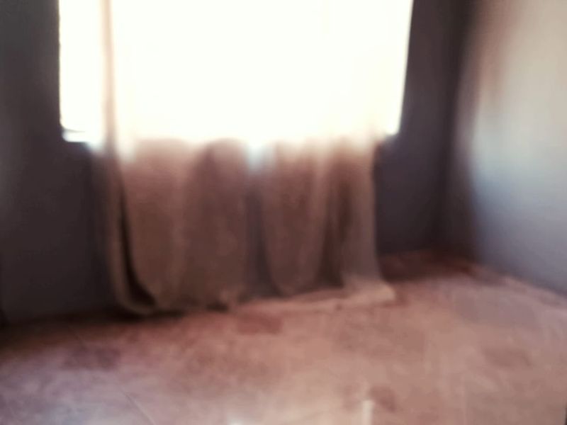 An empty bedroom featuring tiled flooring and a window, currently in need of cosmetic updates.
