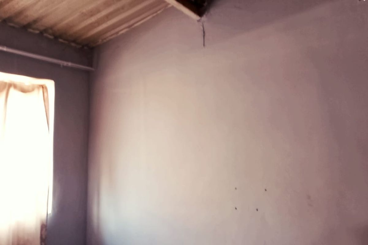 An empty bedroom space featuring an exposed corrugated ceiling and plain walls, requiring cosmetic updates and finishing touches.