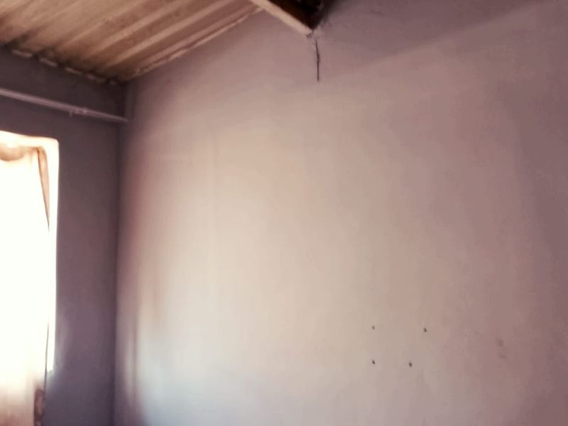 An empty bedroom space featuring an exposed corrugated ceiling and plain walls, requiring cosmetic updates and finishing touches.