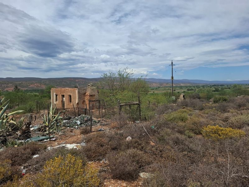 A view of a vacant residential plot featuring a dilapidated structure, utility pole, and natural landscape with surrounding mountain views.