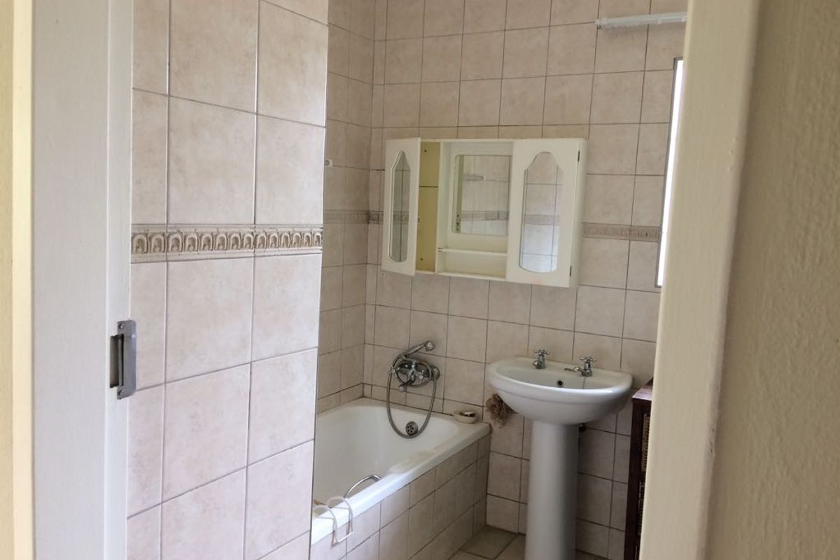 A functional bathroom featuring a pedestal basin, built-in bathtub, and wall-mounted medicine cabinet with neutral ceramic tiling throughout.