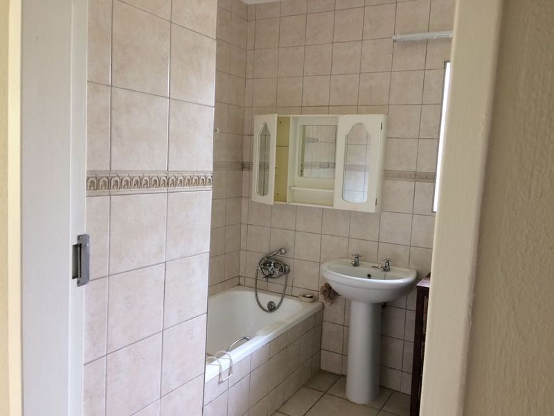 A functional bathroom featuring a pedestal basin, built-in bathtub, and wall-mounted medicine cabinet with neutral ceramic tiling throughout.