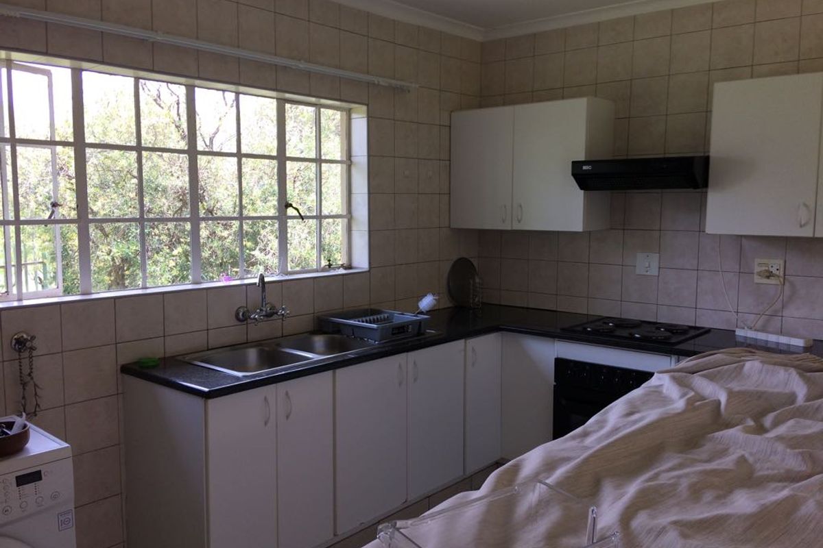 A functional kitchen featuring tiled walls, built-in cabinetry, a double basin sink, and integrated cooking appliances with a window overlooking the garden.
