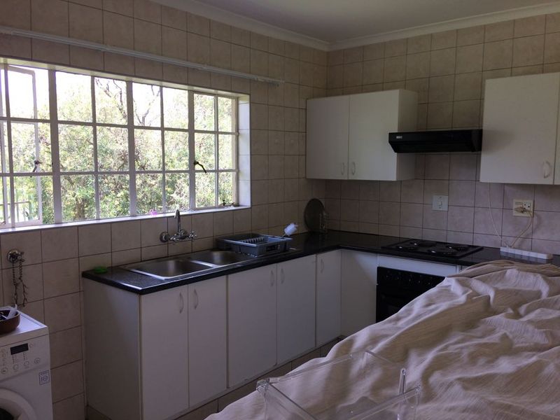 A functional kitchen featuring tiled walls, built-in cabinetry, a double basin sink, and integrated cooking appliances with a window overlooking the garden.