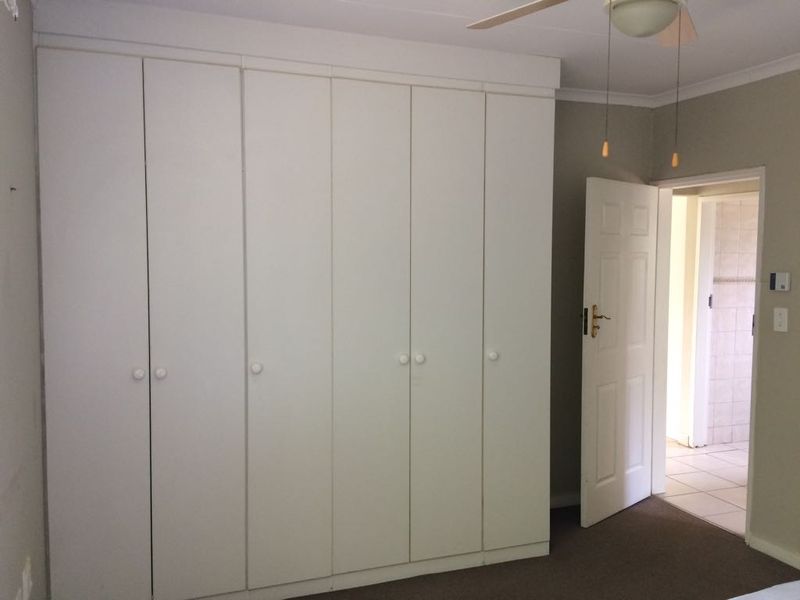 A bedroom featuring extensive built-in cupboards, a ceiling fan, and neutral wall finishes, with an adjacent doorway leading to a tiled area.