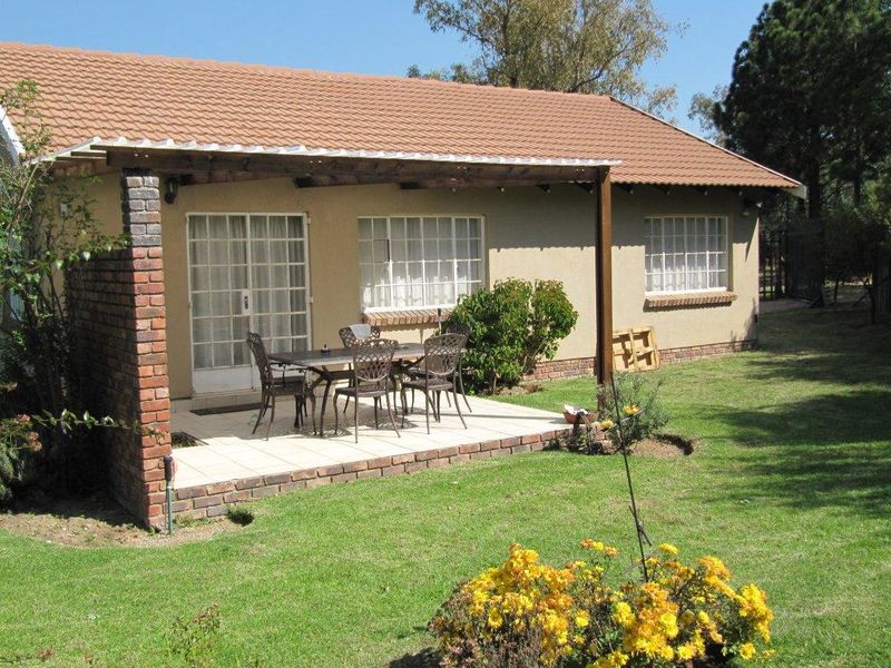 Rear view of the house featuring a covered tiled patio, brick pillar support, and a well-maintained garden area.