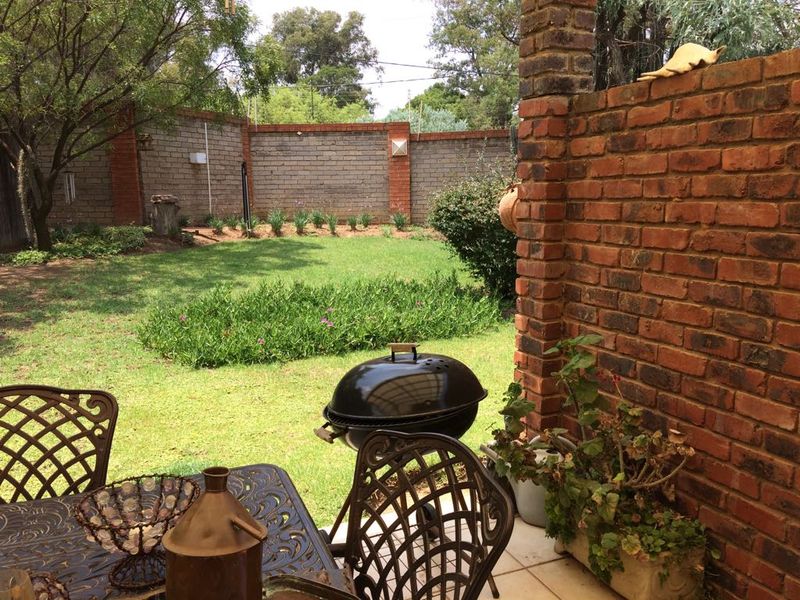 A covered patio area featuring brick masonry walls and pillars, overlooking a private garden with established lawn and perimeter boundary walls.