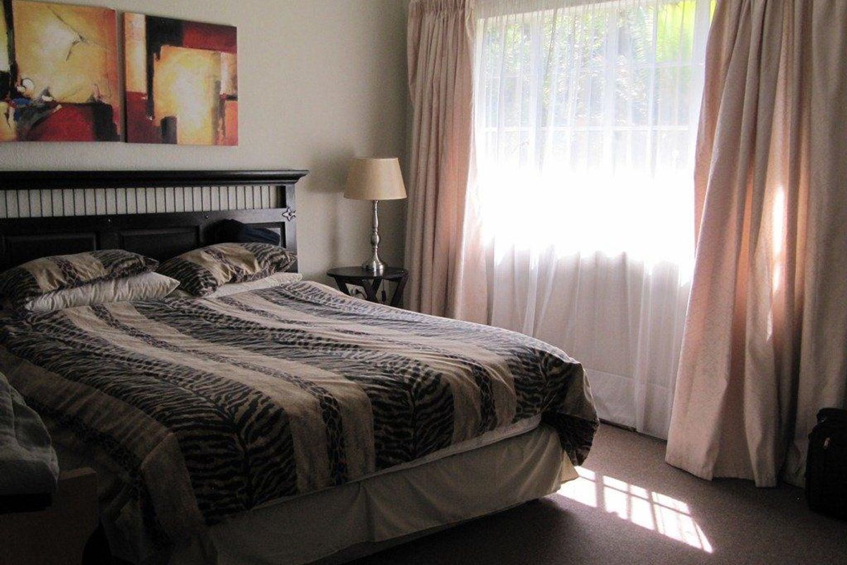 A comfortable bedroom featuring carpeted flooring and large windows with curtain treatments, providing natural light and a functional living space.