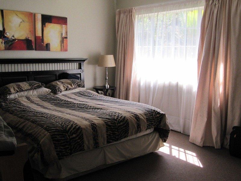 A comfortable bedroom featuring carpeted flooring and large windows with curtain treatments, providing natural light and a functional living space.