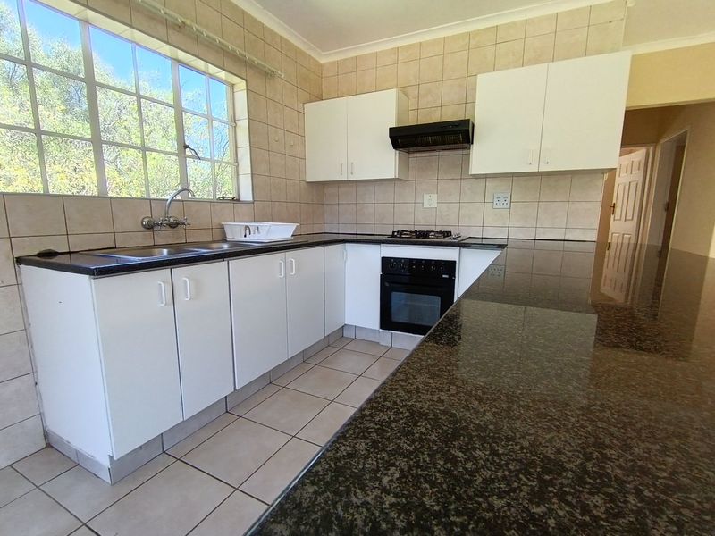 A functional kitchen featuring granite countertops, built-in oven with gas hob, extractor fan, and ample cabinetry, finished with tiled splashbacks and flooring.