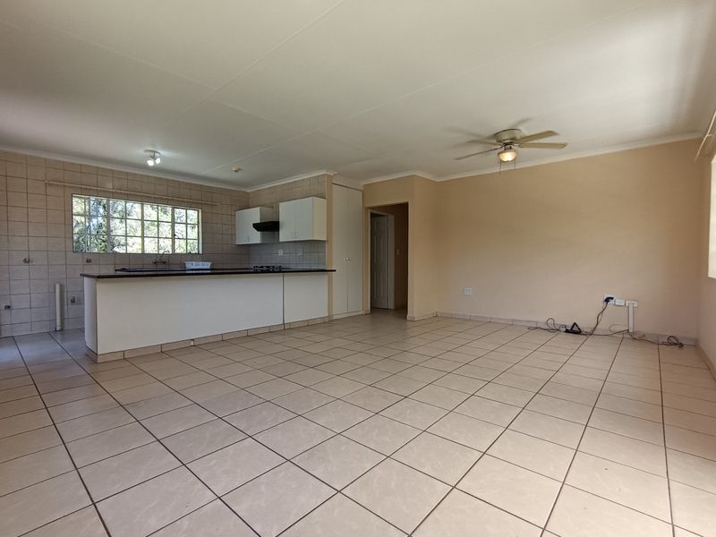 Spacious open-plan living area featuring tiled flooring, a functional kitchen island with built-in cabinetry, and a ceiling fan in a neutral setting.