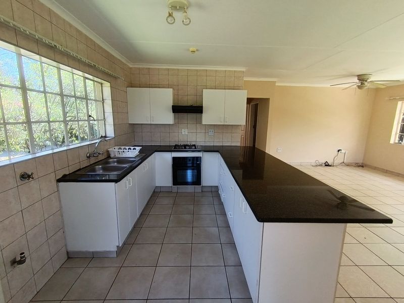 Open plan kitchen featuring granite countertops, built-in oven, gas hob, and tiled flooring, flowing into an adjacent living area.