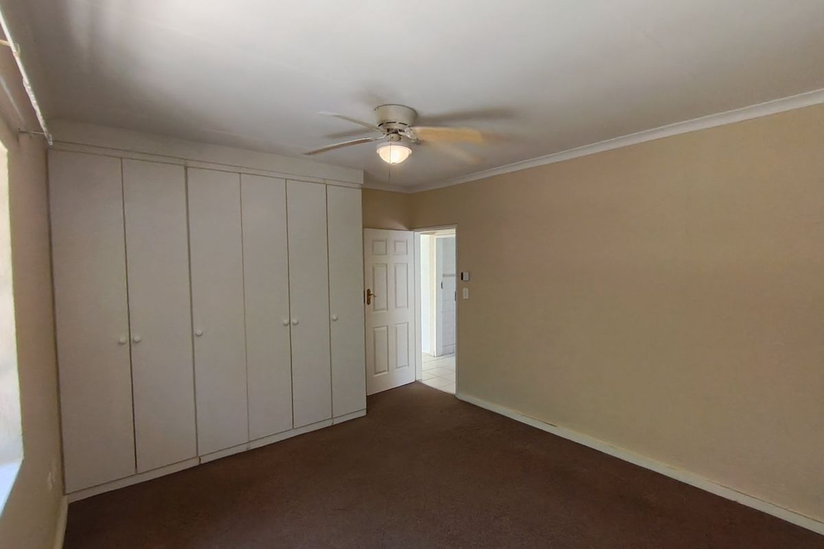 A spacious, empty bedroom featuring neutral walls, carpeted flooring, and extensive built-in cupboard storage with a ceiling fan.