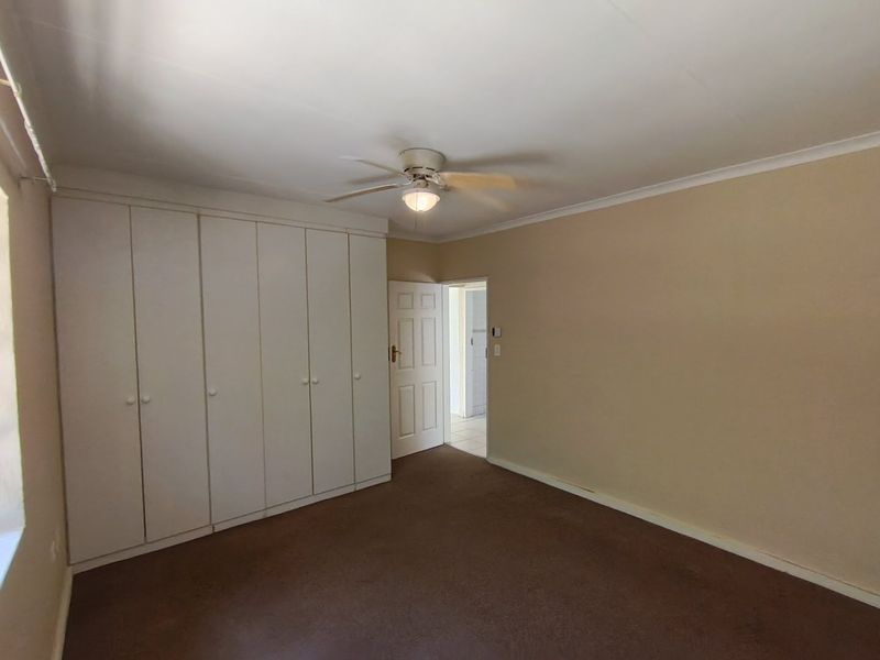 A spacious, empty bedroom featuring neutral walls, carpeted flooring, and extensive built-in cupboard storage with a ceiling fan.