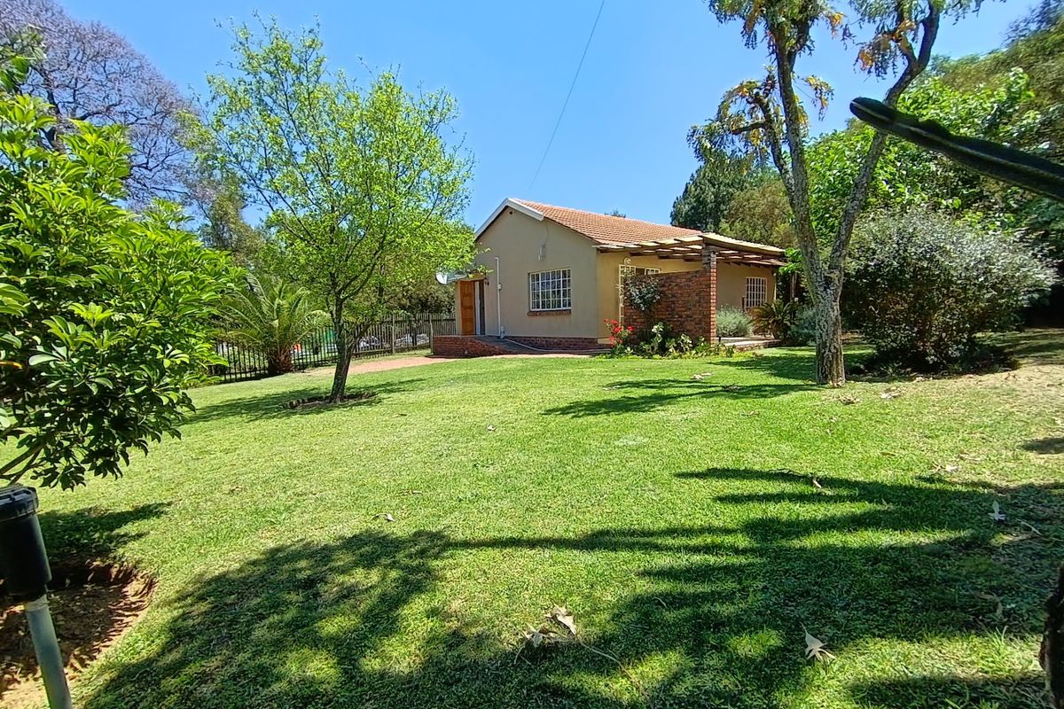 A view of the rear exterior of the house featuring a well-maintained lawn, mature trees, and a covered patio area with a timber pergola.